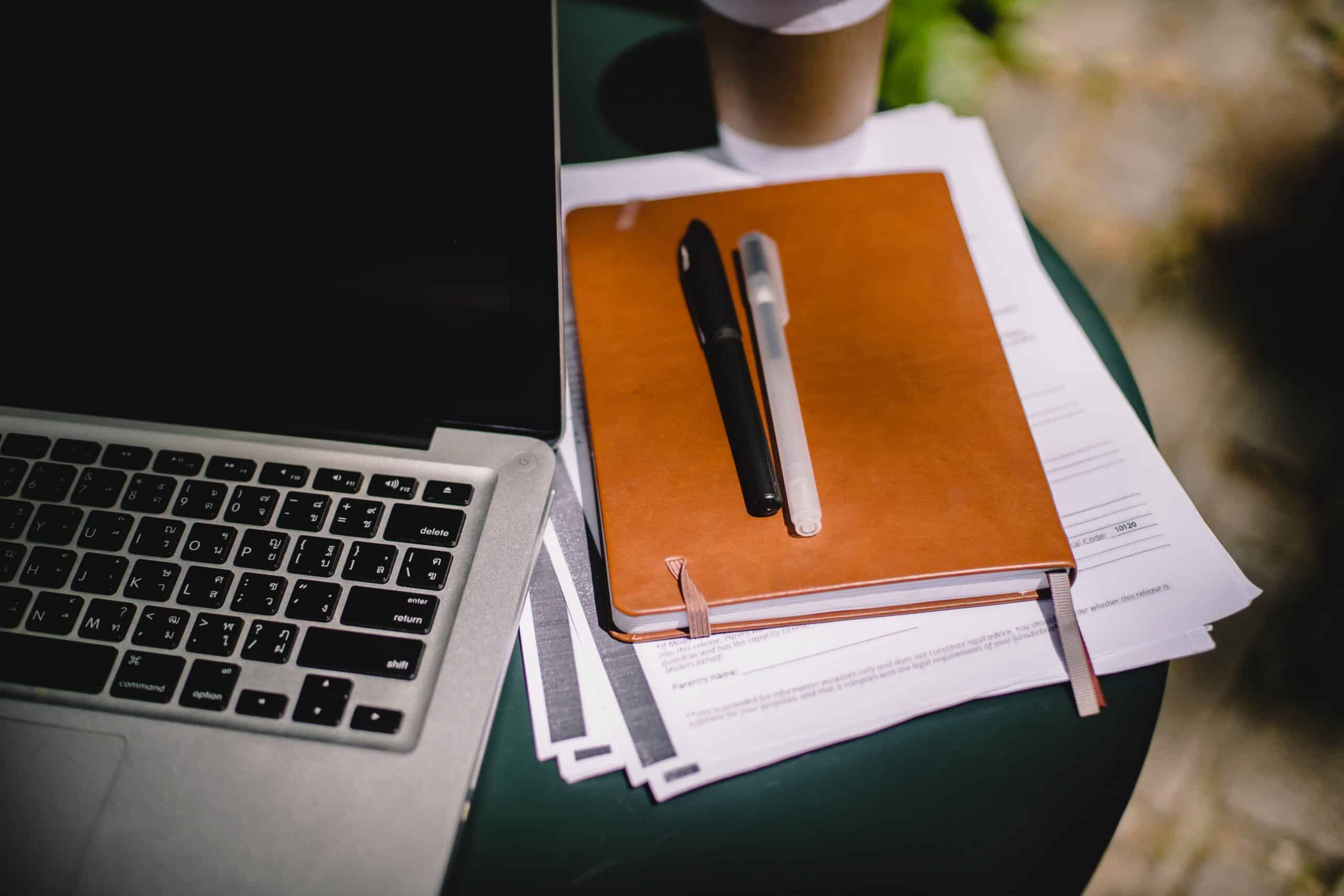 Laptop opened with a notebook and stack of papers next to it.