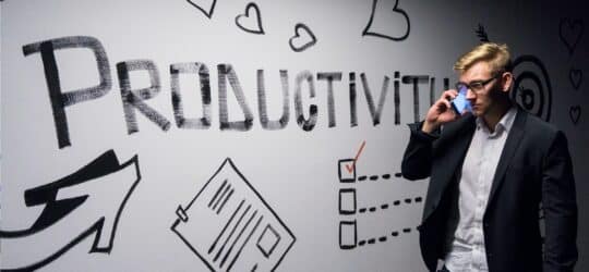 Man in a suit on the phone standing in front of a wall that says productivity.