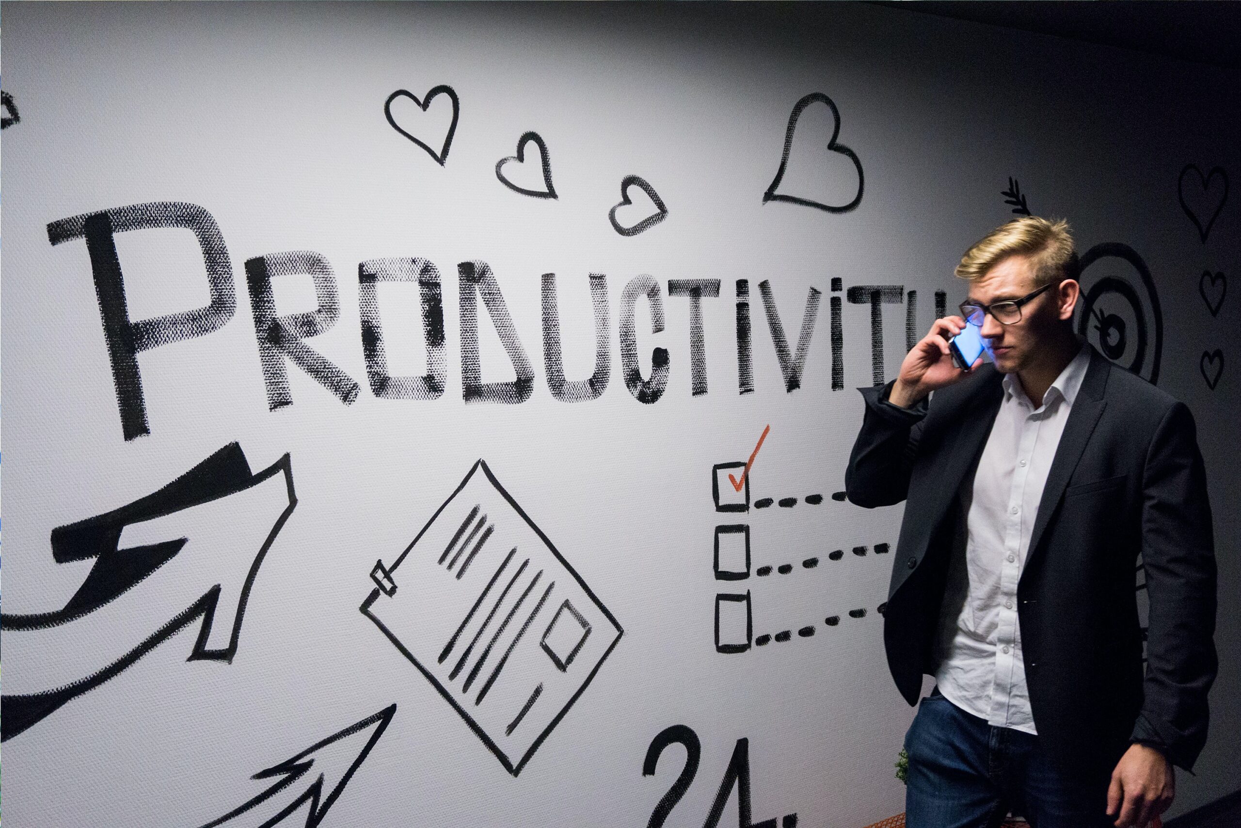 Man in a suit on the phone standing in front of a wall that says productivity.