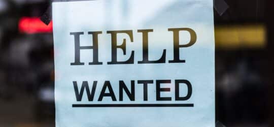 Help wanted sign hanging in the storefront window.