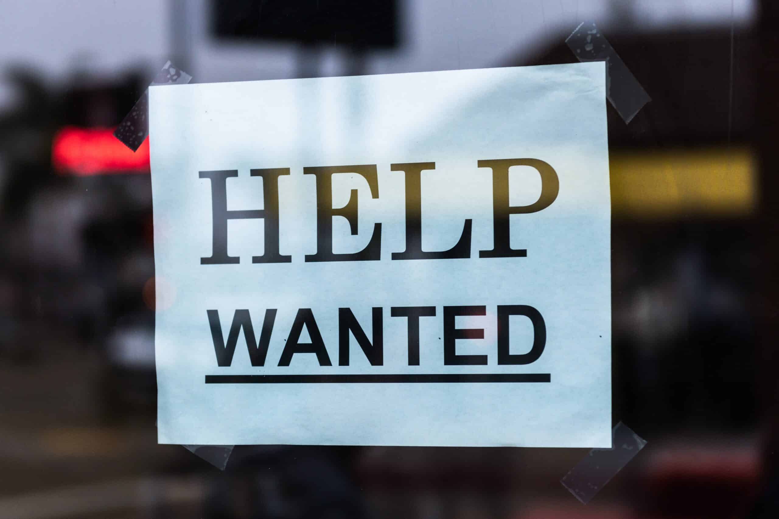 Help wanted sign hanging in the storefront window.