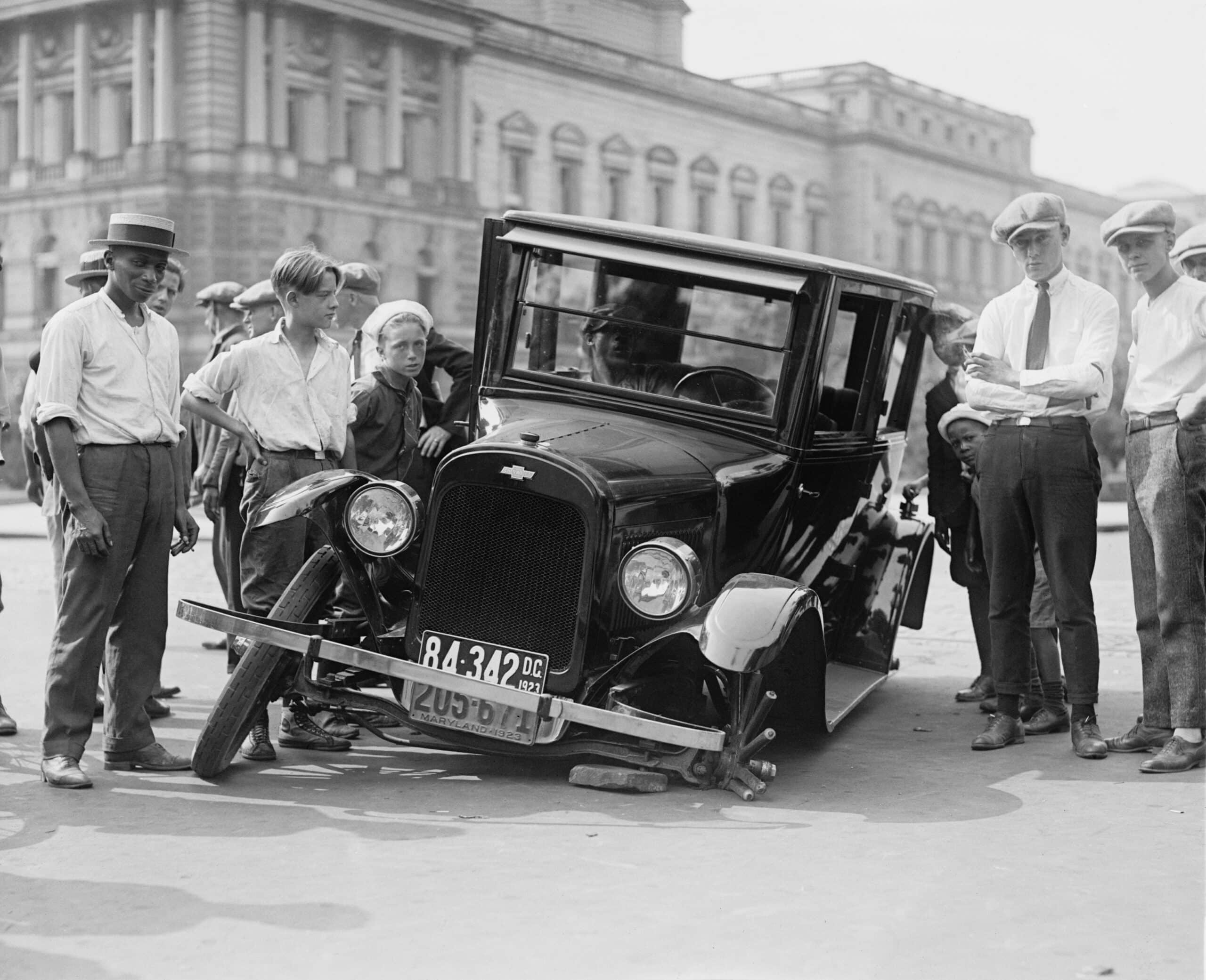 Grayscale Photo of People Standing near the Wrecked Vintage Car