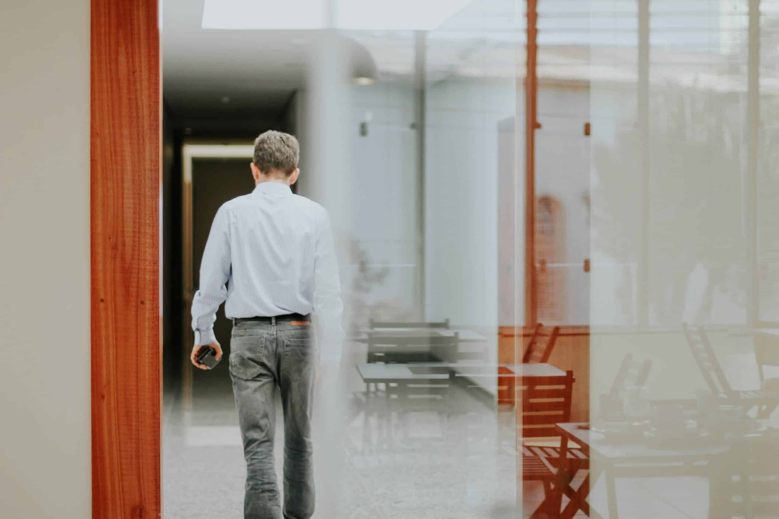 man in white dress shirt and gray denim jeans standing in front of glass window